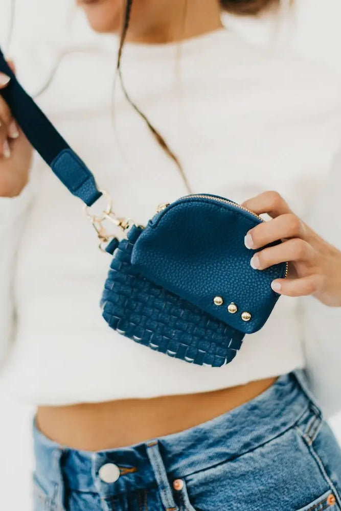 Person holding a blue handbag with a textured strap against a white background