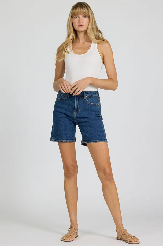 Woman wearing a white tank top and blue denim shorts on a plain background