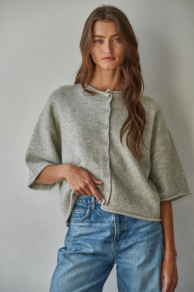 Woman wearing a light gray cardigan and blue jeans against a plain background