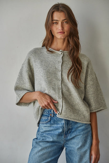 Woman wearing a light gray cardigan and blue jeans against a plain background