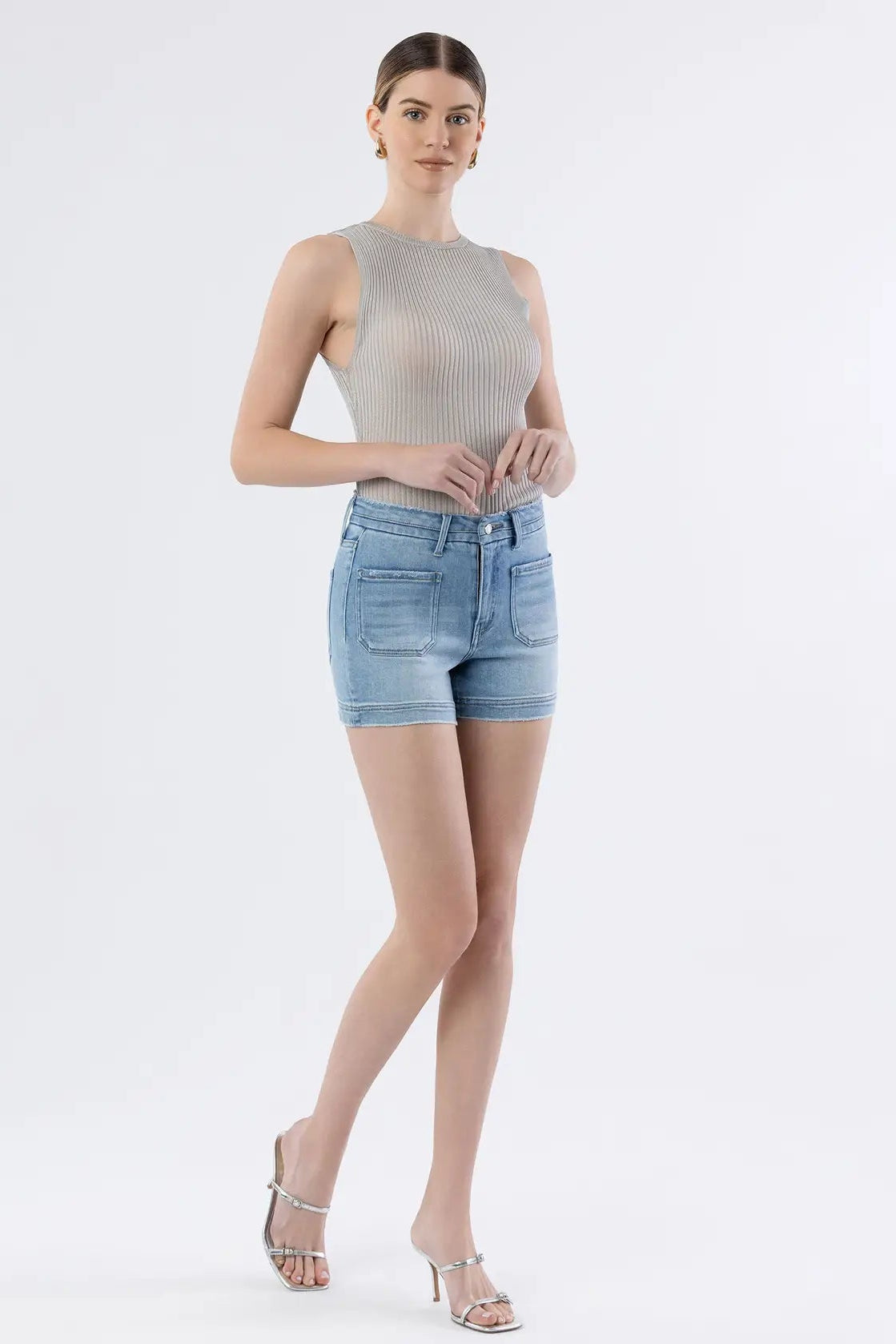 Woman wearing a gray sleeveless top and light blue denim shorts on a white background