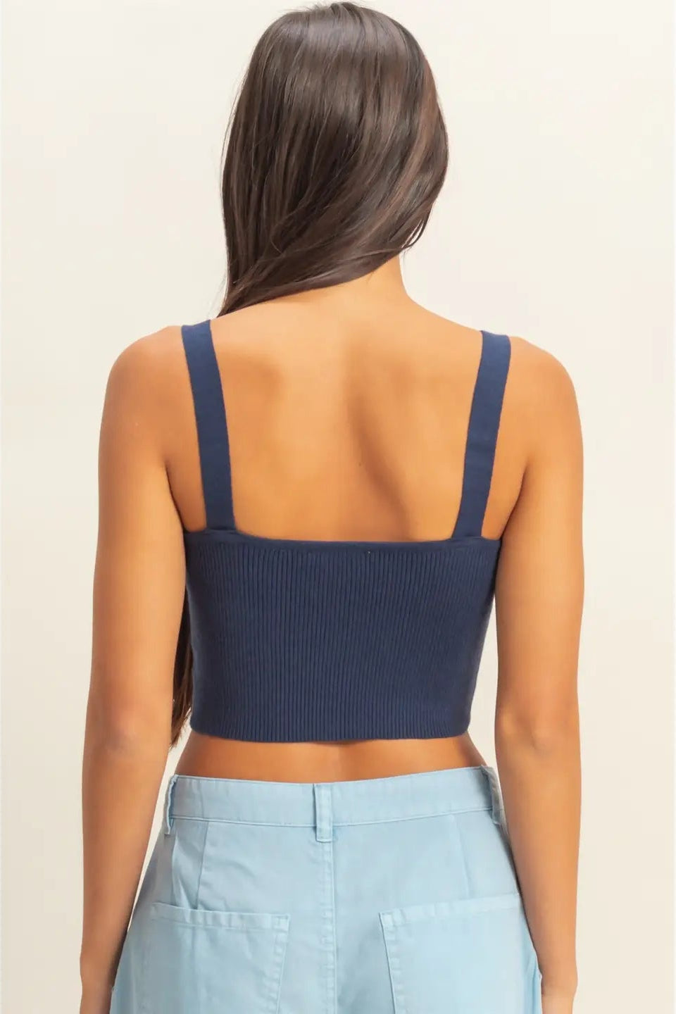 Woman wearing a navy blue crop top and light blue pants on a beige background