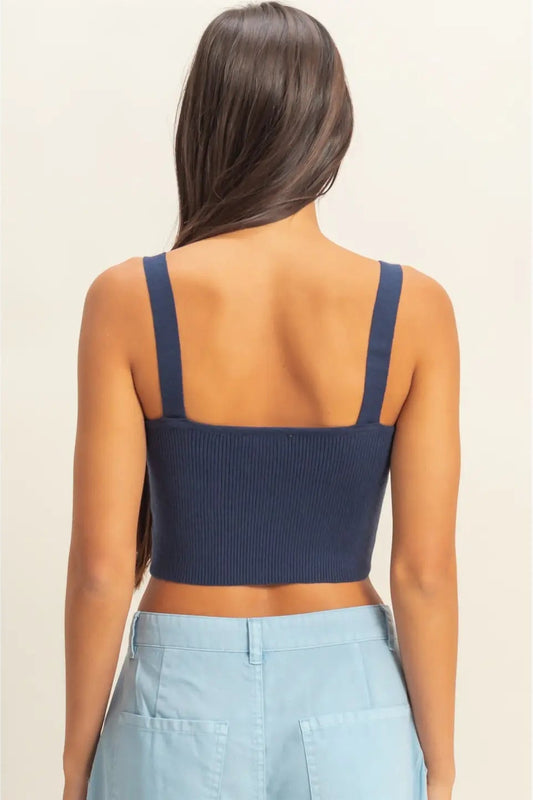 Woman wearing a navy blue crop top and light blue pants on a beige background