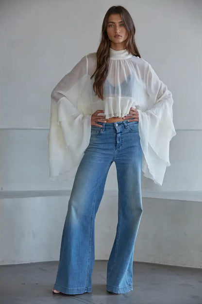Woman wearing a white layered scarf and blue jeans against a plain background