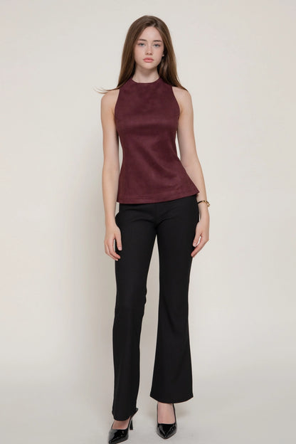 A woman modeling a sleeveless high-neck satin top in deep burgundy paired with black pants and black heels, standing against a plain light beige studio background.