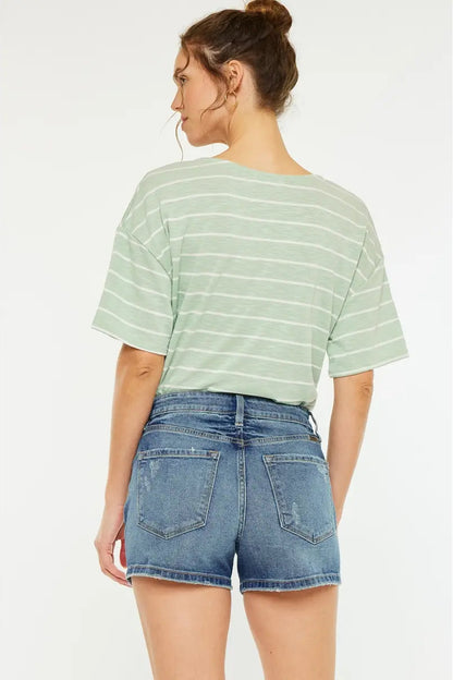 Person wearing a green striped shirt and denim shorts on a white background