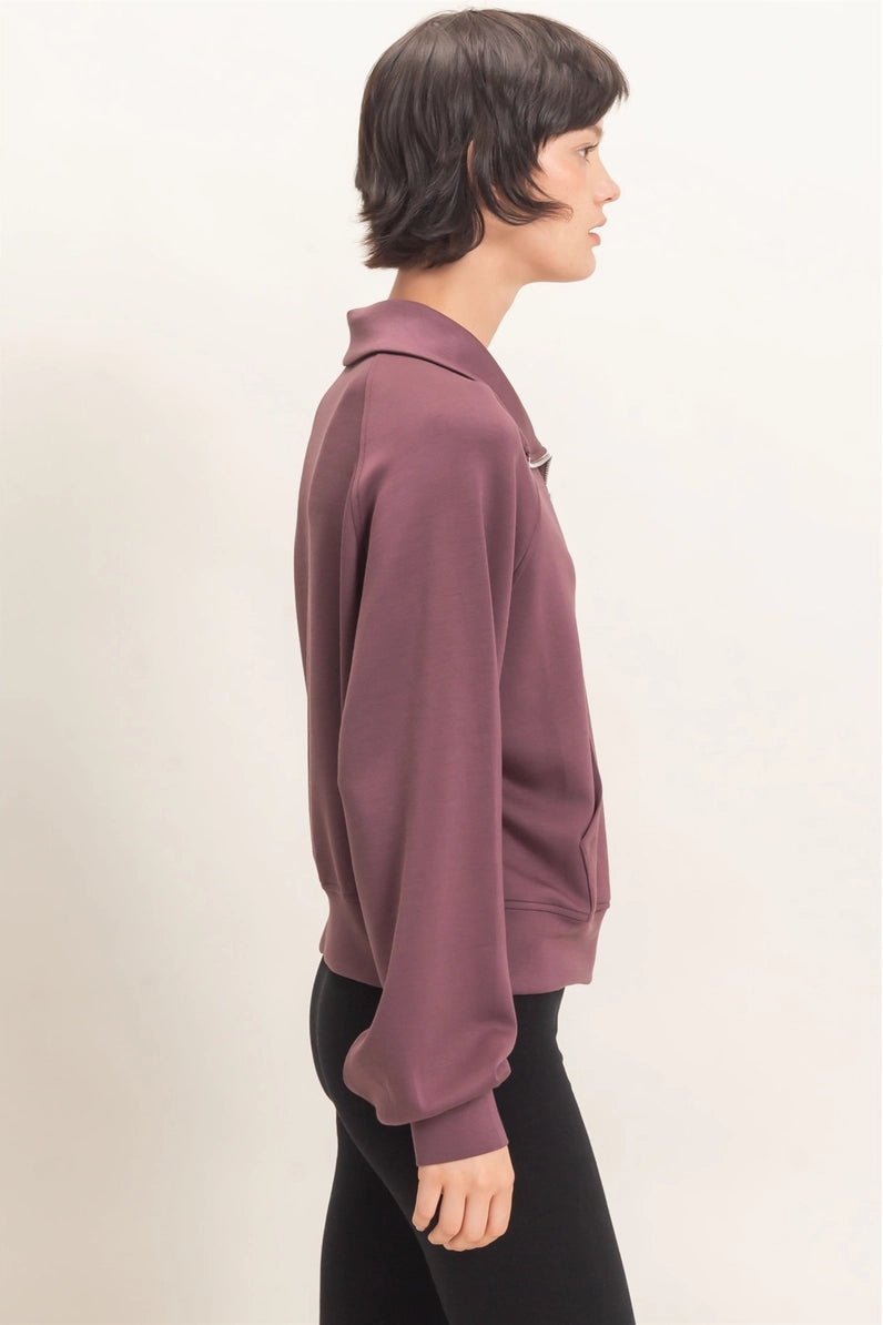Person wearing a mauve hoodie and black pants on a light beige background