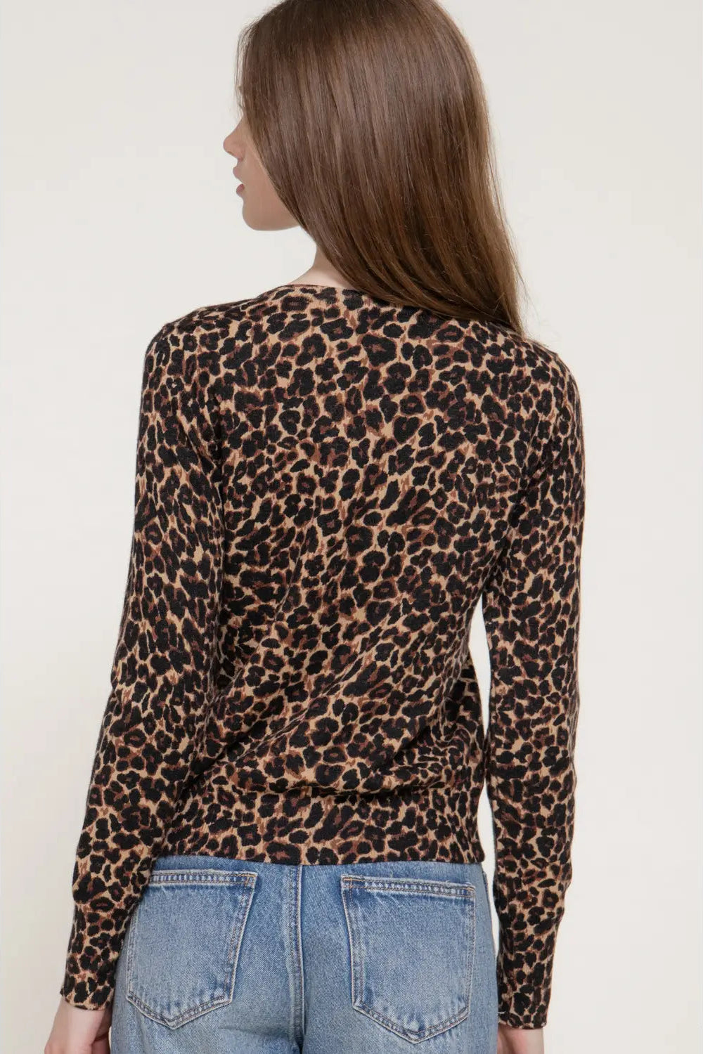 A woman shown from the back wearing a leopard print long-sleeve top and light blue jeans against a plain light background.