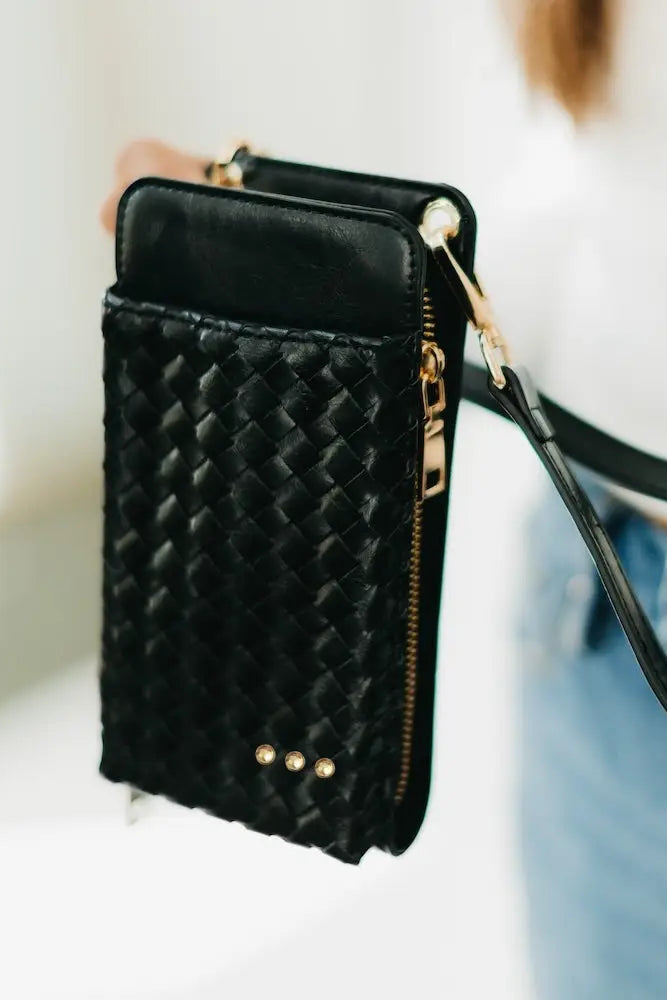 Black quilted phone case with gold accents held by a person wearing a white shirt and blue jeans.