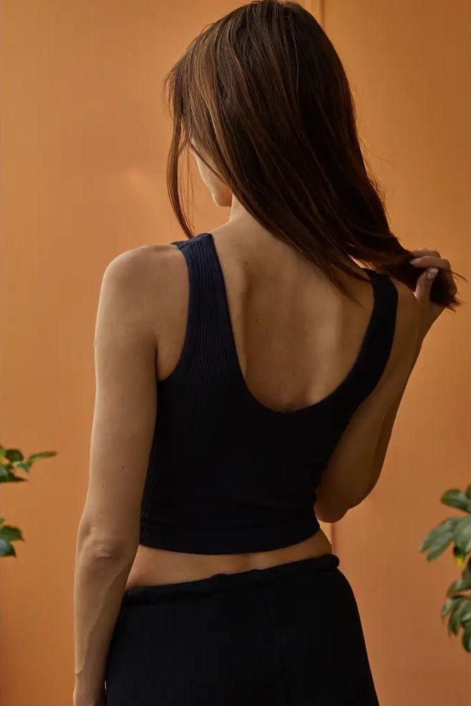 Woman wearing a black sports bra and leggings against an orange wall.