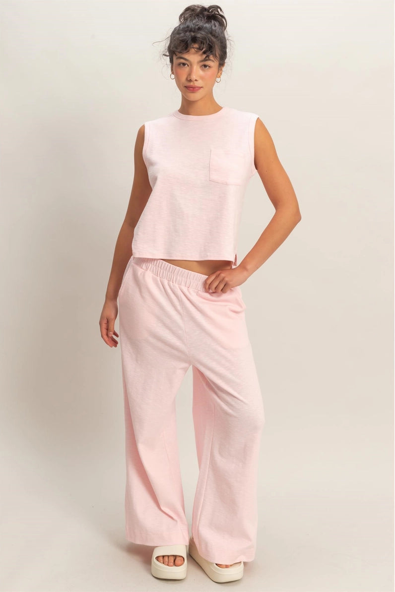 Woman wearing a pink sleeveless top and pants on a plain background