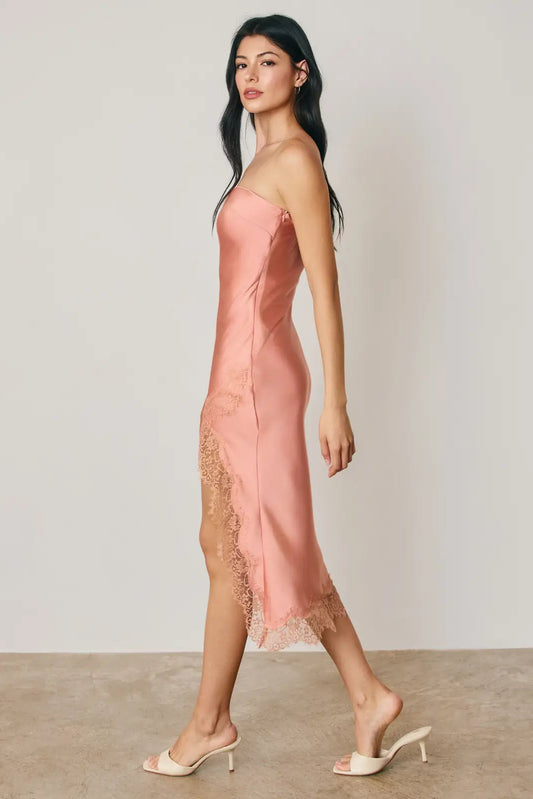 Woman wearing a pink satin dress with lace details on a plain background