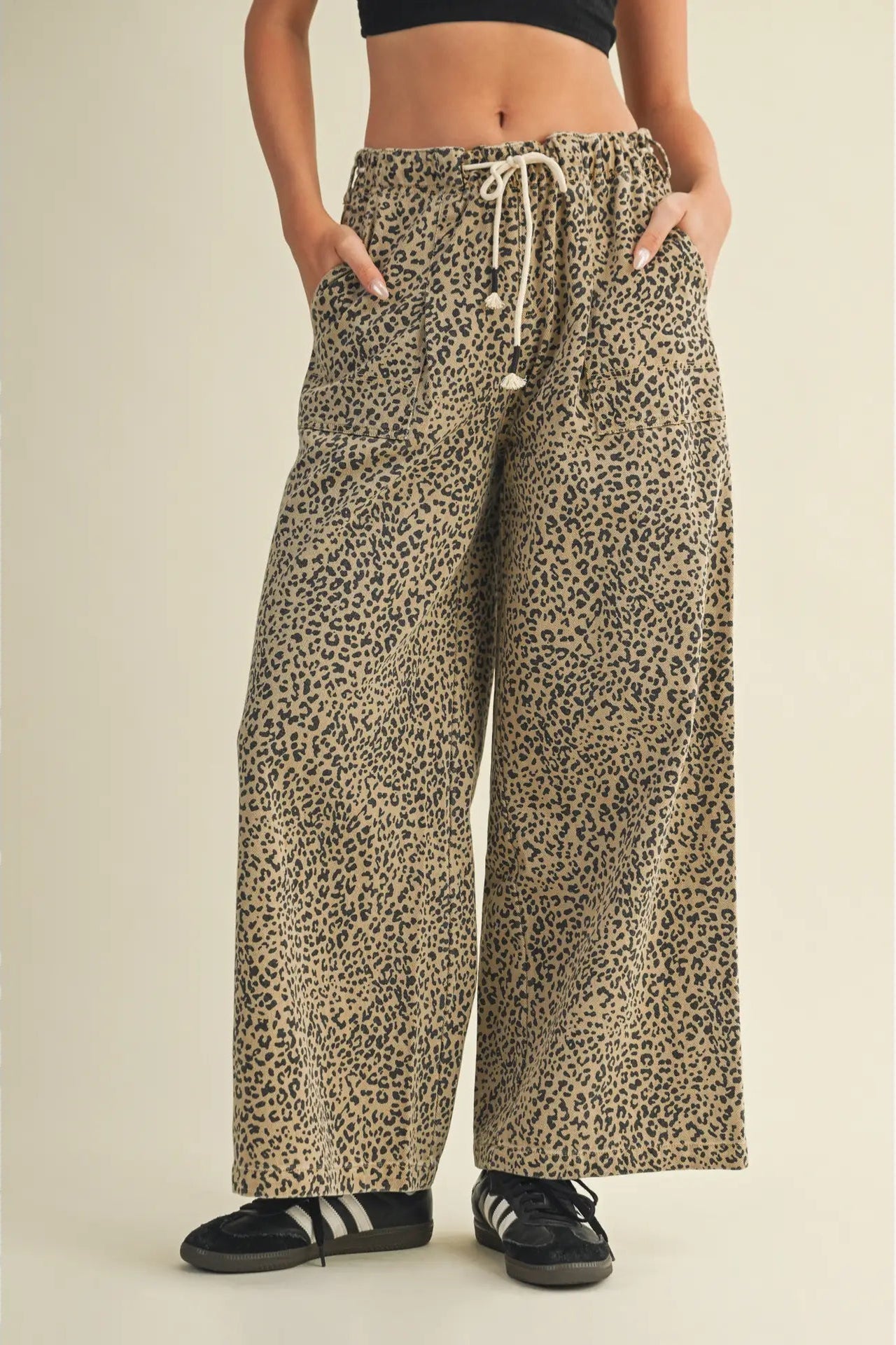 A person wearing loose, wide-leg leopard-print pants with a drawstring waist, shown from the torso down against a plain beige studio background.