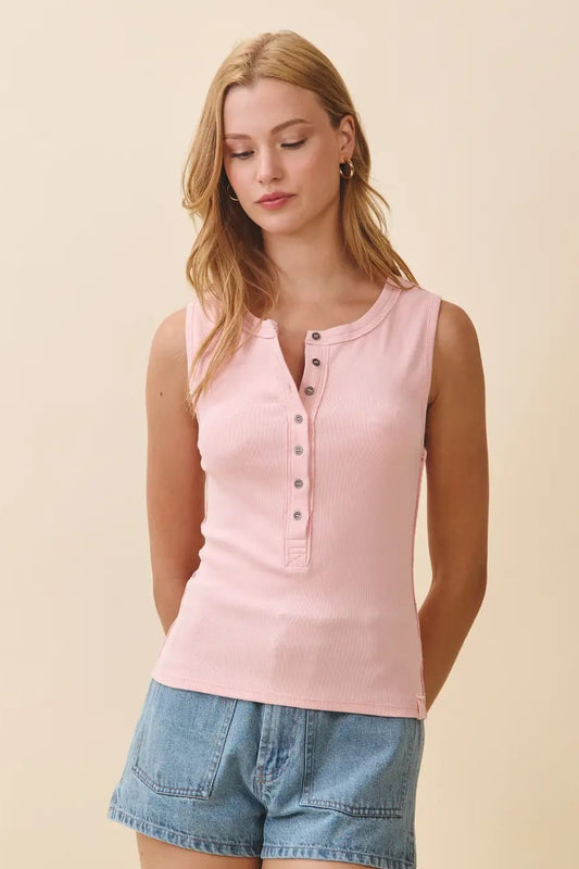 Woman wearing a pink sleeveless top and denim shorts against a beige background