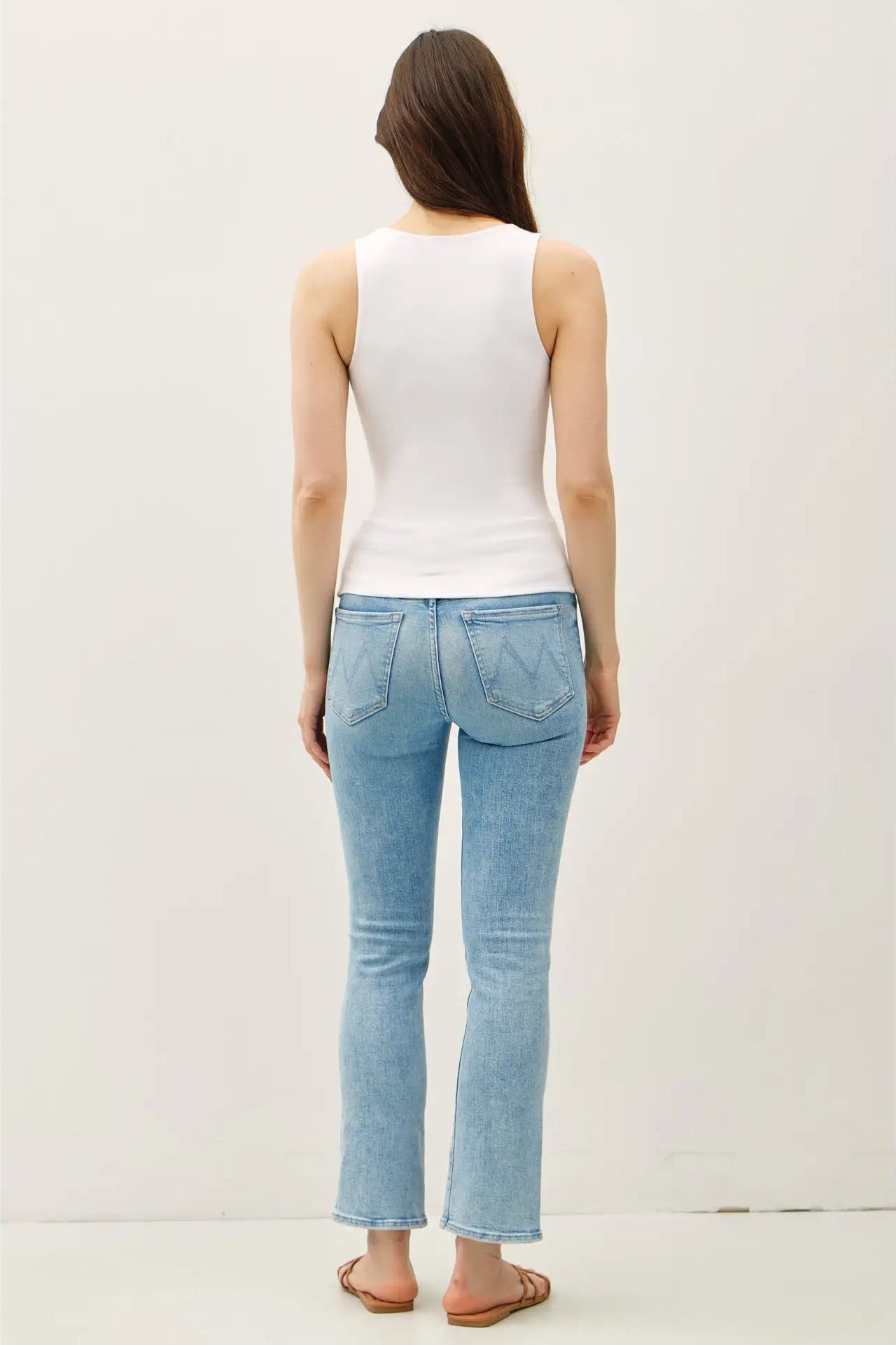 Woman wearing light blue jeans and a white top on a plain background