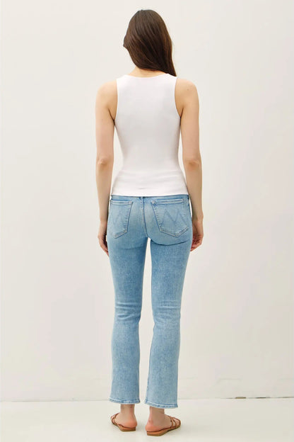 Woman wearing light blue jeans and a white top on a plain background