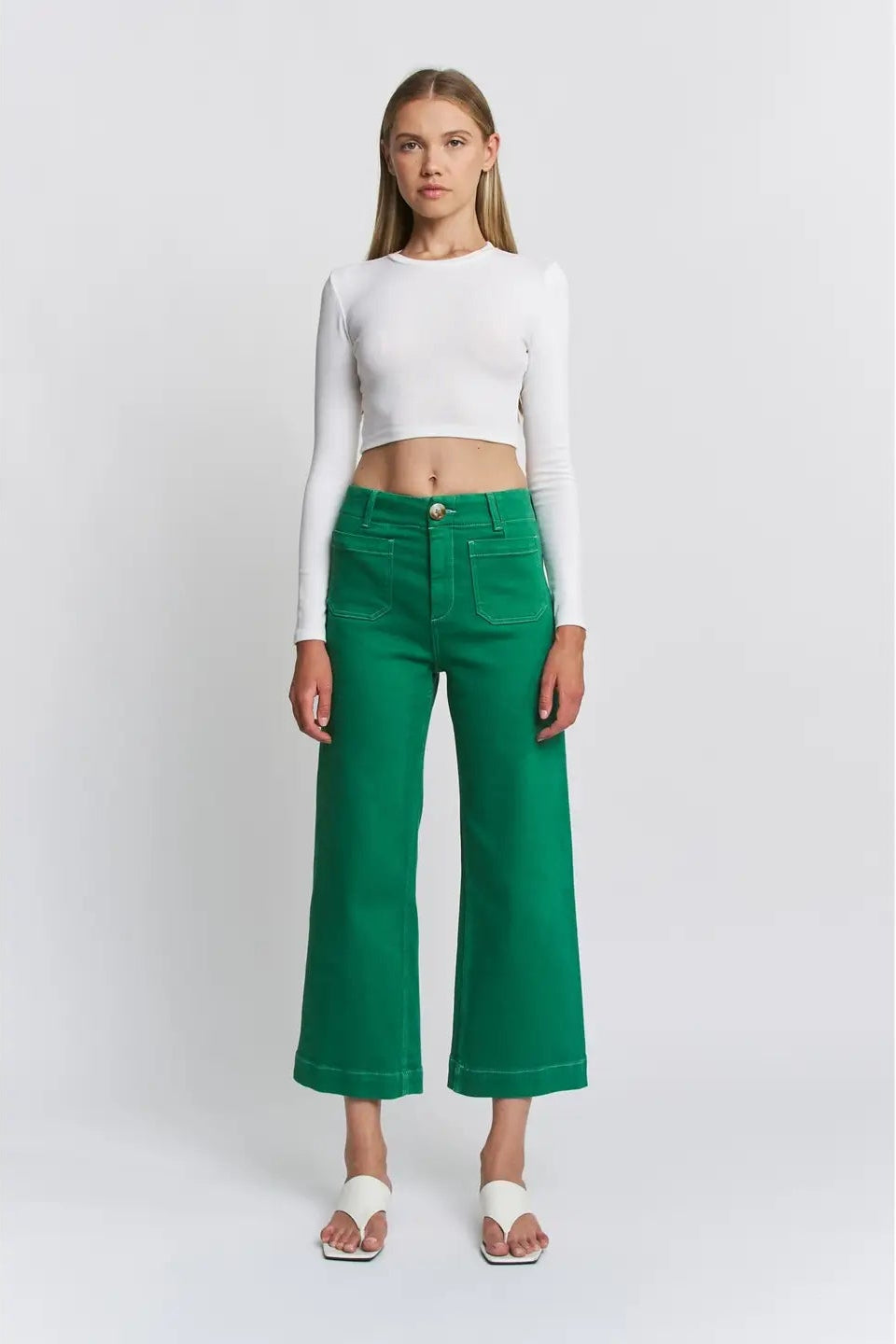 Woman wearing a white crop top and green pants on a white background