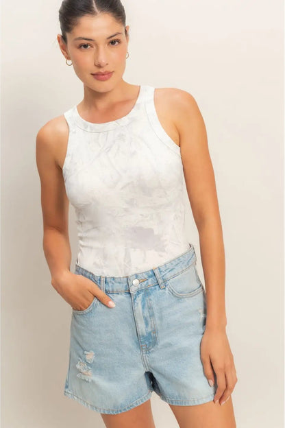 Woman wearing a white sleeveless top and light blue denim shorts against a plain background