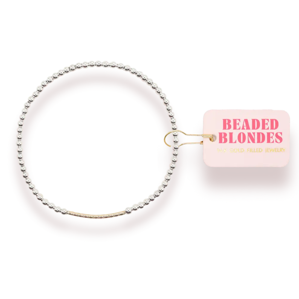 A delicate beaded bangle bracelet with a gold-toned center band, shown on a white background with a pink tag that reads 'BEADED BLONDES'.