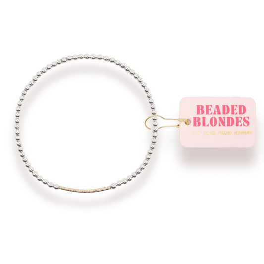 A delicate beaded bangle bracelet with a gold-toned center band, shown on a white background with a pink tag that reads 'BEADED BLONDES'.