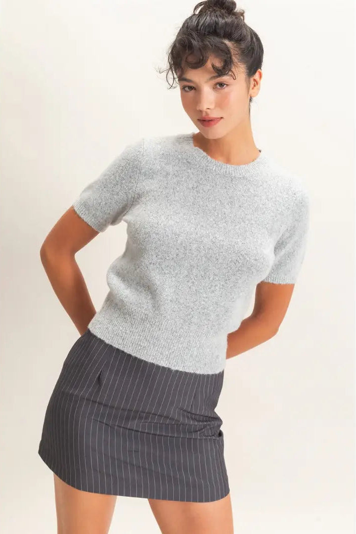 A woman modeling a light gray short-sleeve knit top and a dark gray pinstriped mini skirt against a plain off-white studio background.