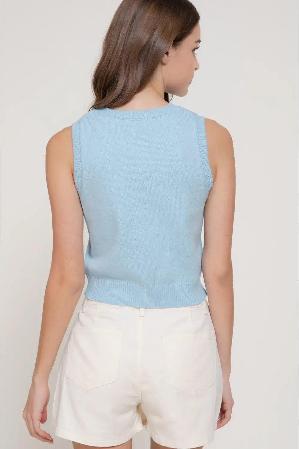 Woman wearing a light blue sleeveless top and white shorts on a plain background