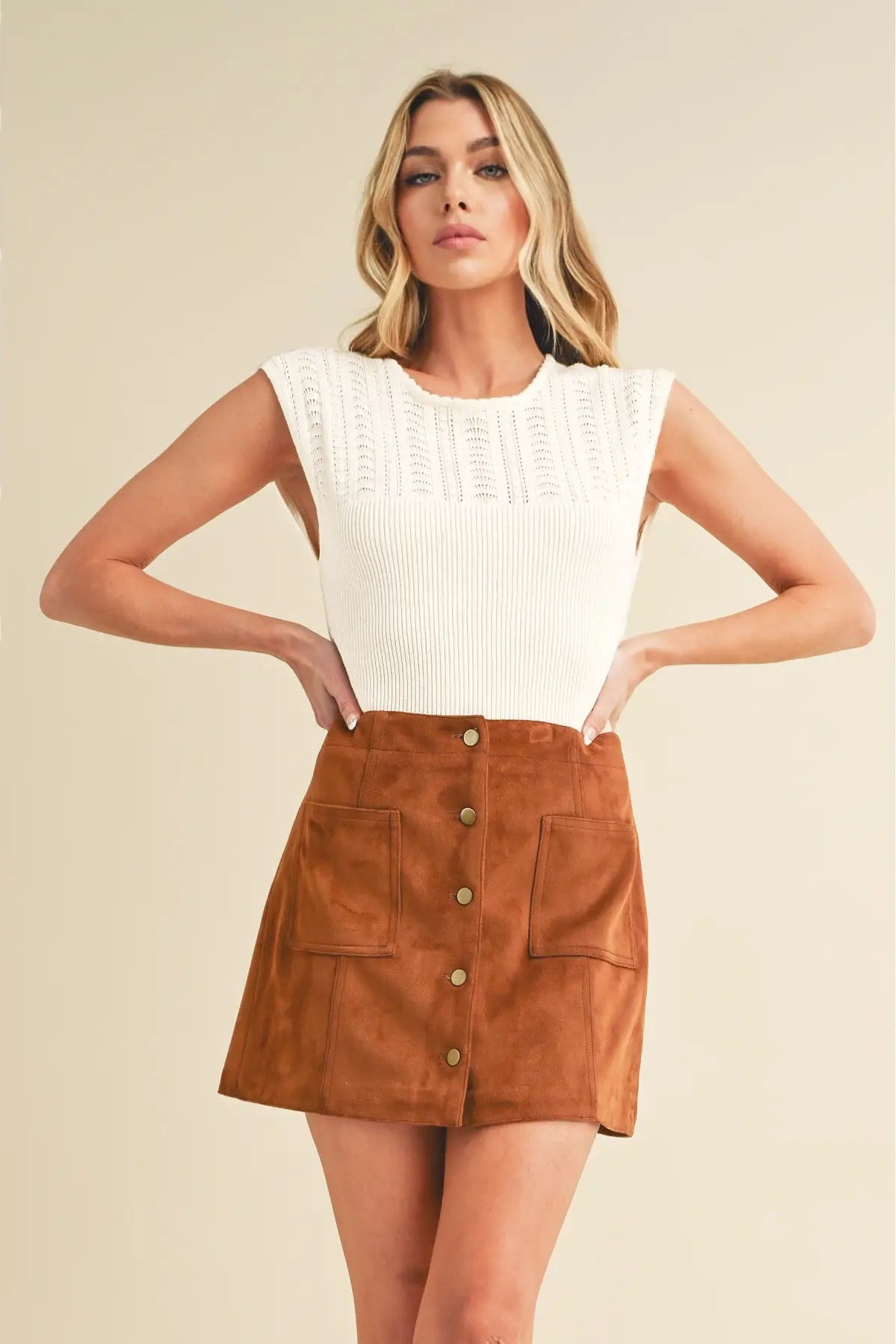Woman wearing a white top and brown suede skirt on a beige background