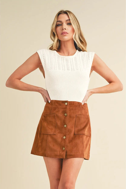 Woman wearing a white top and brown suede skirt on a beige background