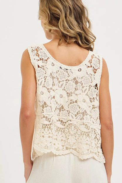 Woman wearing a white lace sleeveless top on a plain background