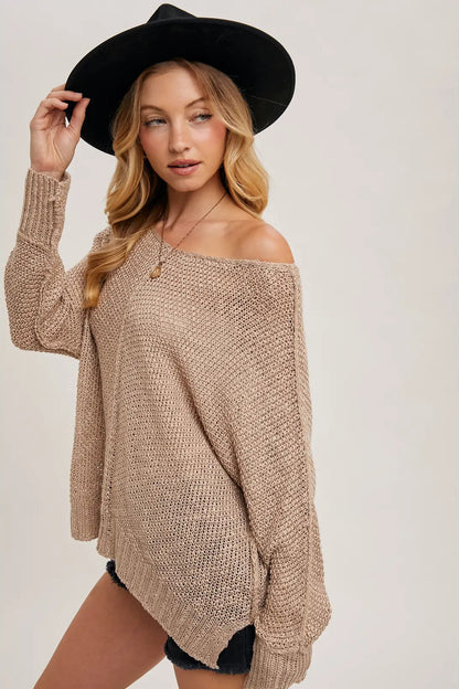 Woman wearing a beige off-shoulder sweater and black hat on a plain background