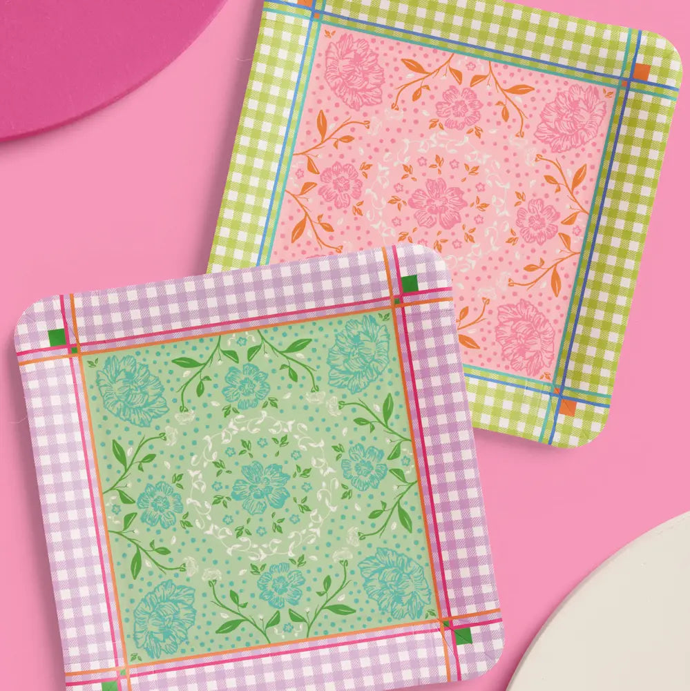 Two decorative square coasters with rounded corners displayed on a pink background. One coaster has a light green and lavender gingham border with a mint green floral pattern inside, and the other has a pink floral pattern inside with a light green and yellow gingham border.