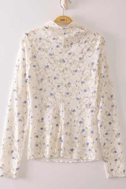 A long-sleeve lace blouse in cream with a blue and green floral pattern, hanging on a wooden hanger labeled 'VERY J' against a light gray background.