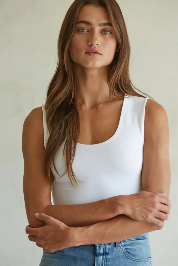 Woman wearing a white tank top and blue jeans against a plain background