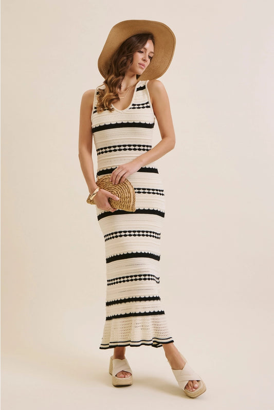 Woman wearing a black and white striped dress with a straw hat and clutch on a beige background