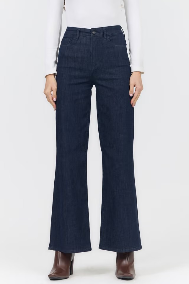 A model wearing dark blue wide-leg flare jeans, paired with a white long-sleeve top and brown ankle boots, shown from the waist down against a plain white background.