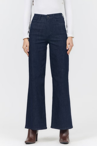A model wearing dark blue wide-leg flare jeans, paired with a white long-sleeve top and brown ankle boots, shown from the waist down against a plain white background.