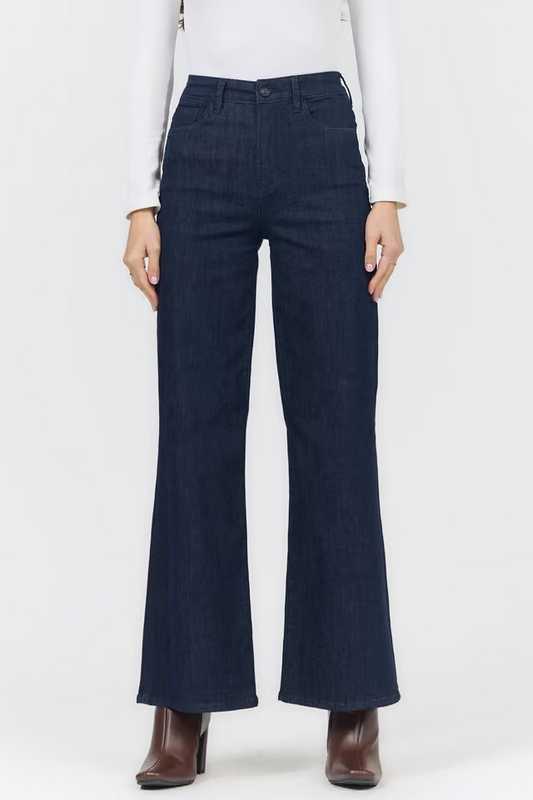 A model wearing dark blue wide-leg flare jeans, paired with a white long-sleeve top and brown ankle boots, shown from the waist down against a plain white background.