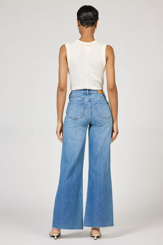 Person wearing a white sleeveless top and blue jeans on a plain background