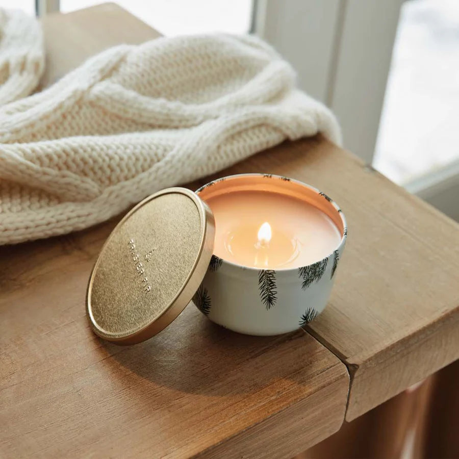 Candle in a decorative container on a wooden surface with a blanket in the background