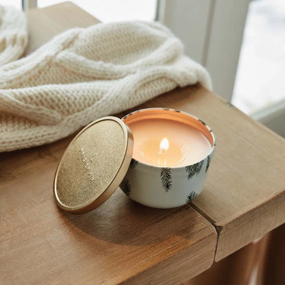 Candle in a decorative container on a wooden surface with a blanket in the background