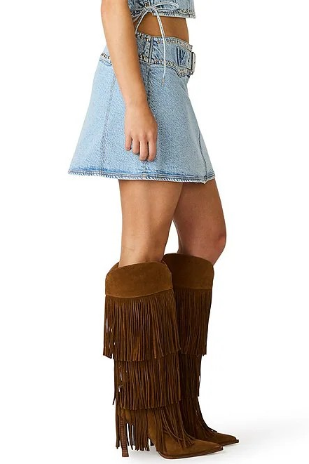 Brown fringed knee-high boots worn with a denim skirt on a white background