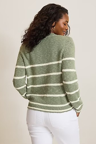 A woman shown from the back wearing a sage green knit sweater with horizontal cream stripes and white pants, photographed against a plain light beige studio background.