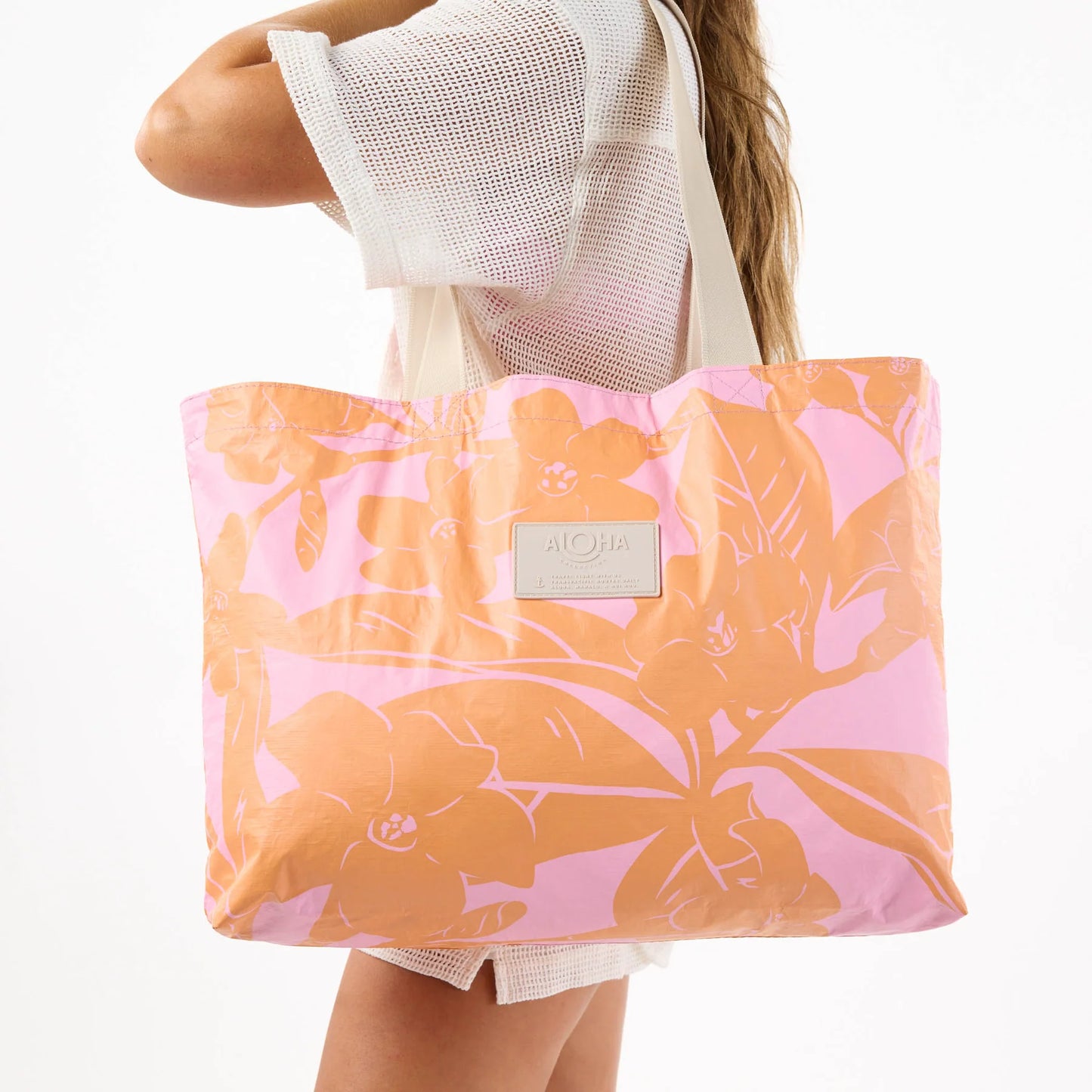 Person holding a pink and orange floral tote bag with a visible brand logo.
