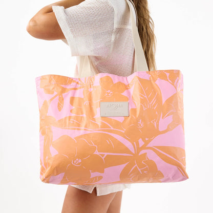 Person holding a pink and orange floral tote bag with a visible brand logo.