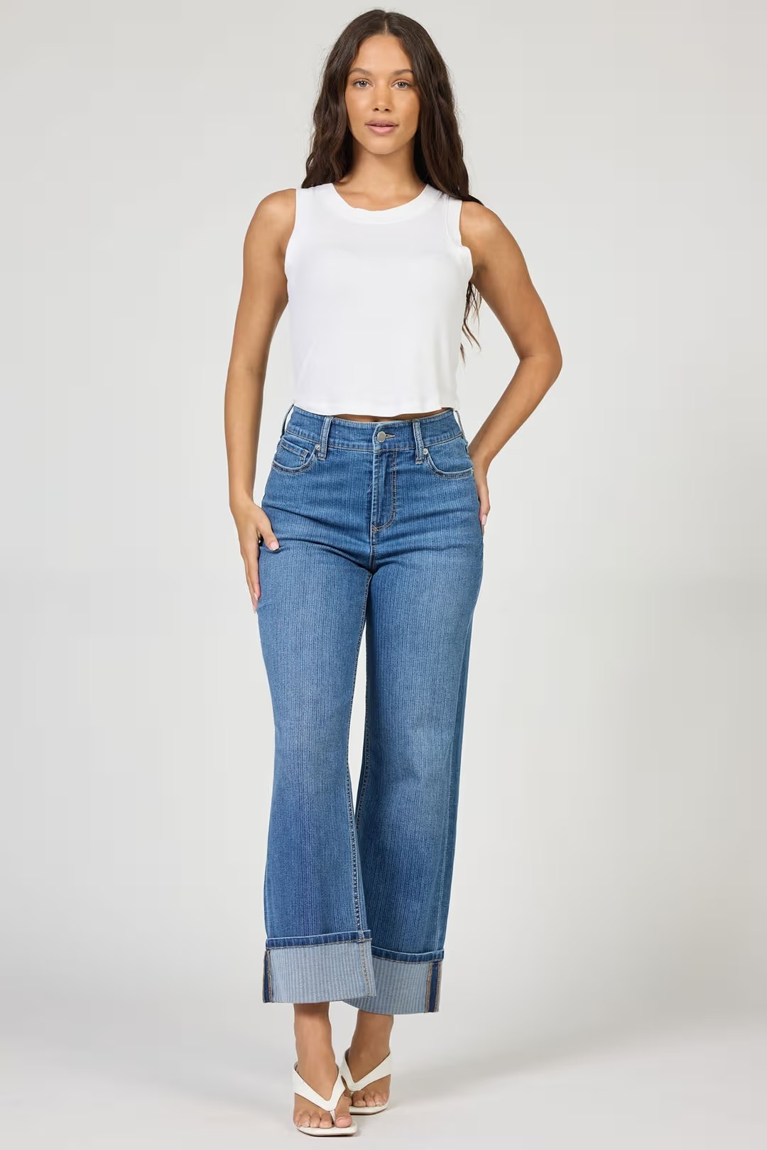 Woman wearing a white sleeveless top and blue jeans on a plain background