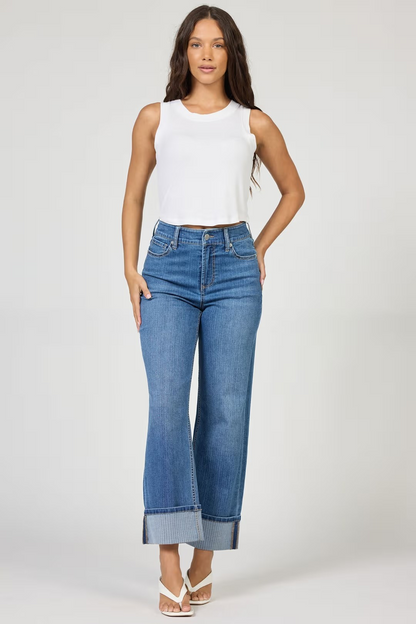 Woman wearing a white sleeveless top and blue jeans on a plain background