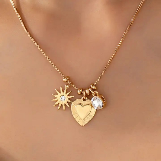 Gold necklace with heart, sun, and round charm on a blurred background