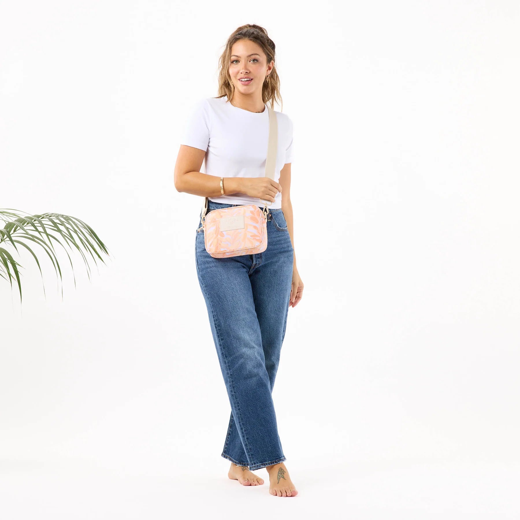 Woman wearing a white shirt and blue jeans with a pink crossbody bag on a white background