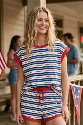 Woman in a striped outfit standing on a wooden porch with American flags.