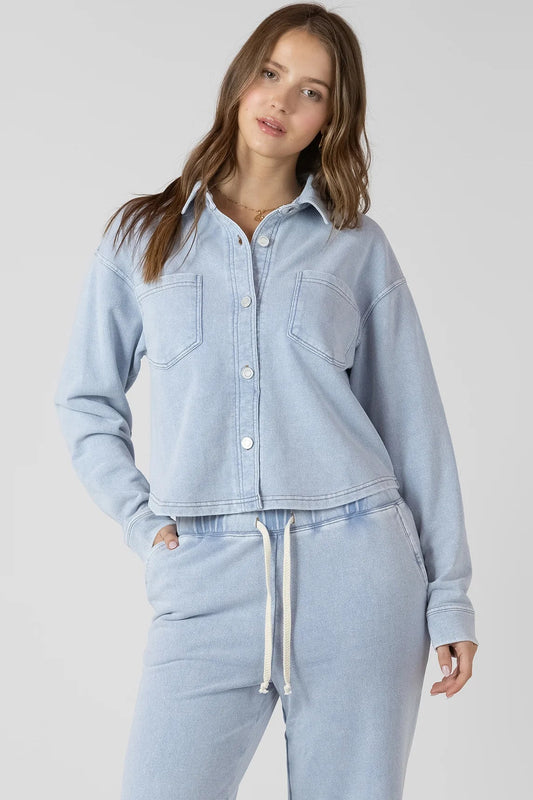 Woman wearing a light blue denim jacket and matching pants on a plain background